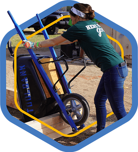 A blue badge showing female Houston ToolBank volunteer dumping dirt from a wheelbarrow