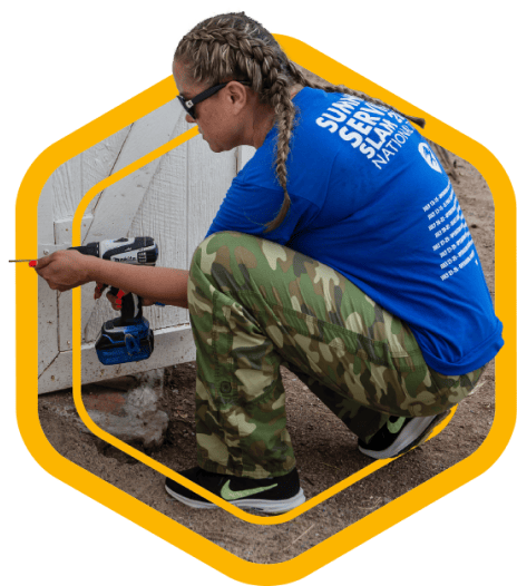 A yellow badge showing a Houston ToolBank volunteer drilling a hole into a barn door