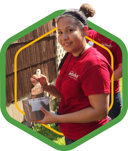 A green badge showing a Methodist volunteer painting a fence