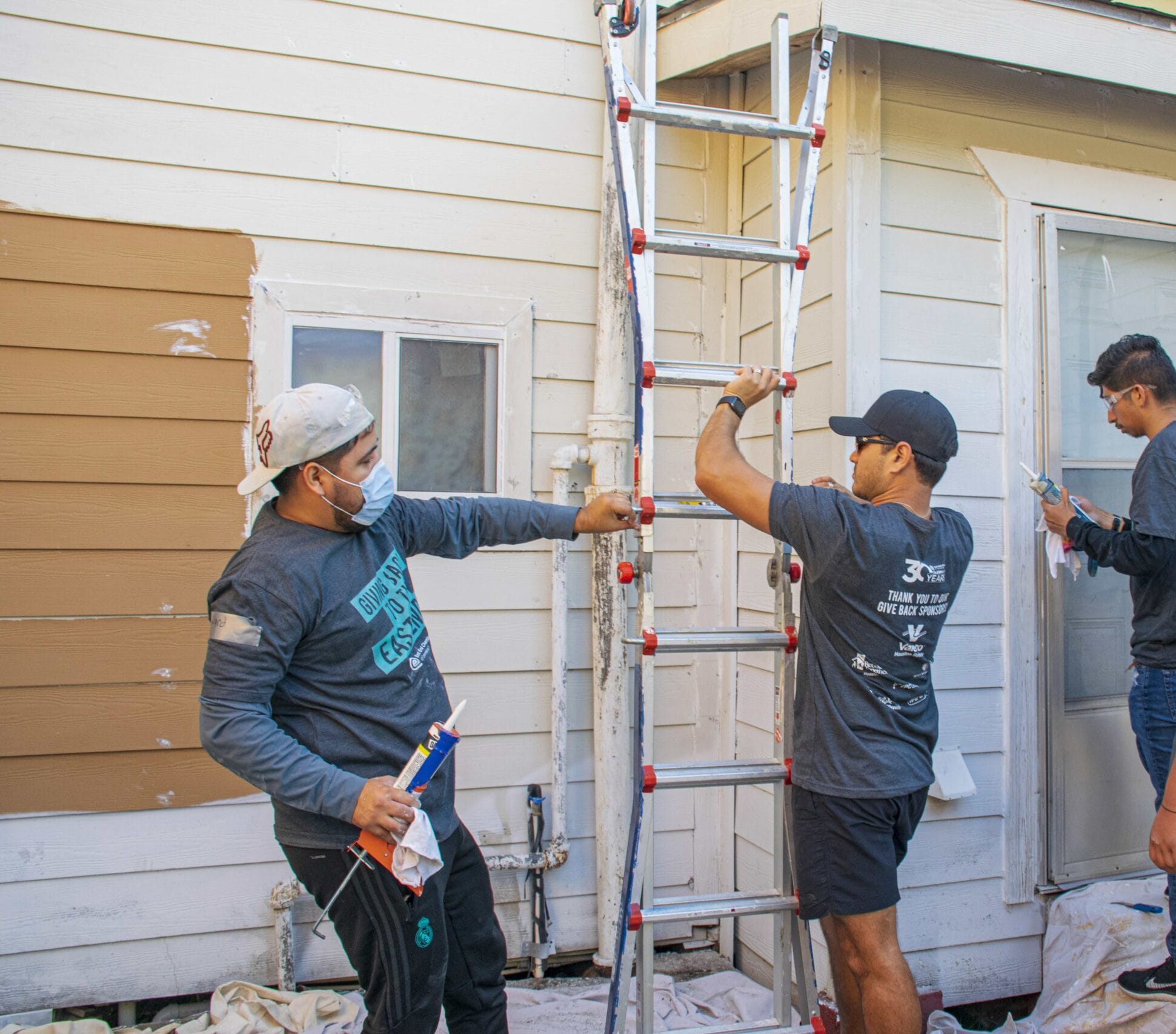 Houston ToolBank volunteers moving a ladder from the side of a house