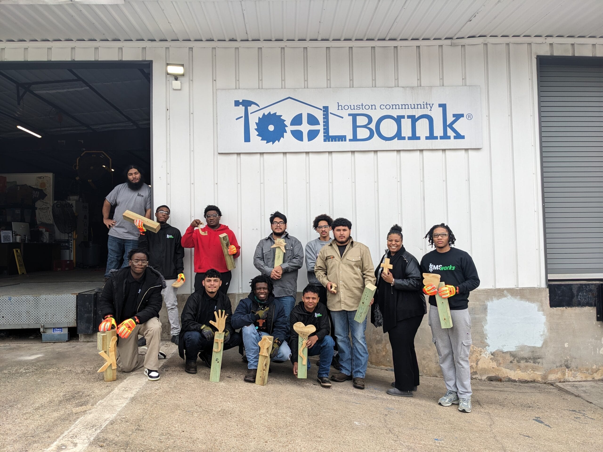 Houston ToolBank volunteers posing outside the warehouse while holding wood projects they made