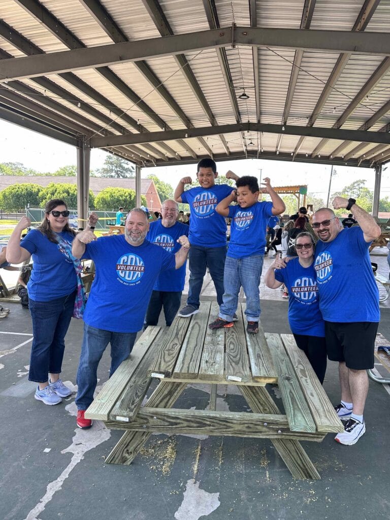 Houston ToolBank volunteers flexing their arms over a completed wooden lunch table