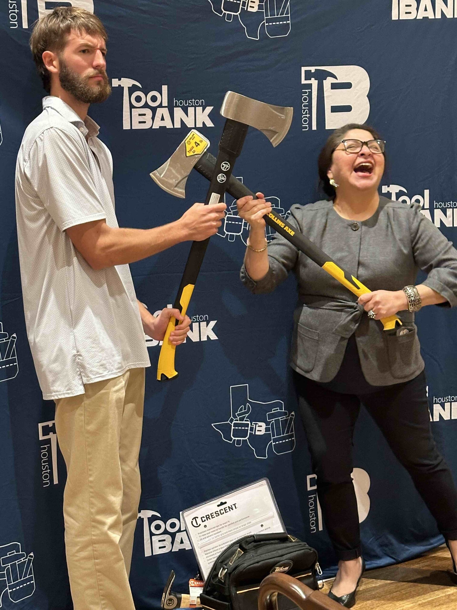 Two Houston ToolBank volunteers posing with axes against a Houston ToolBank backdrop