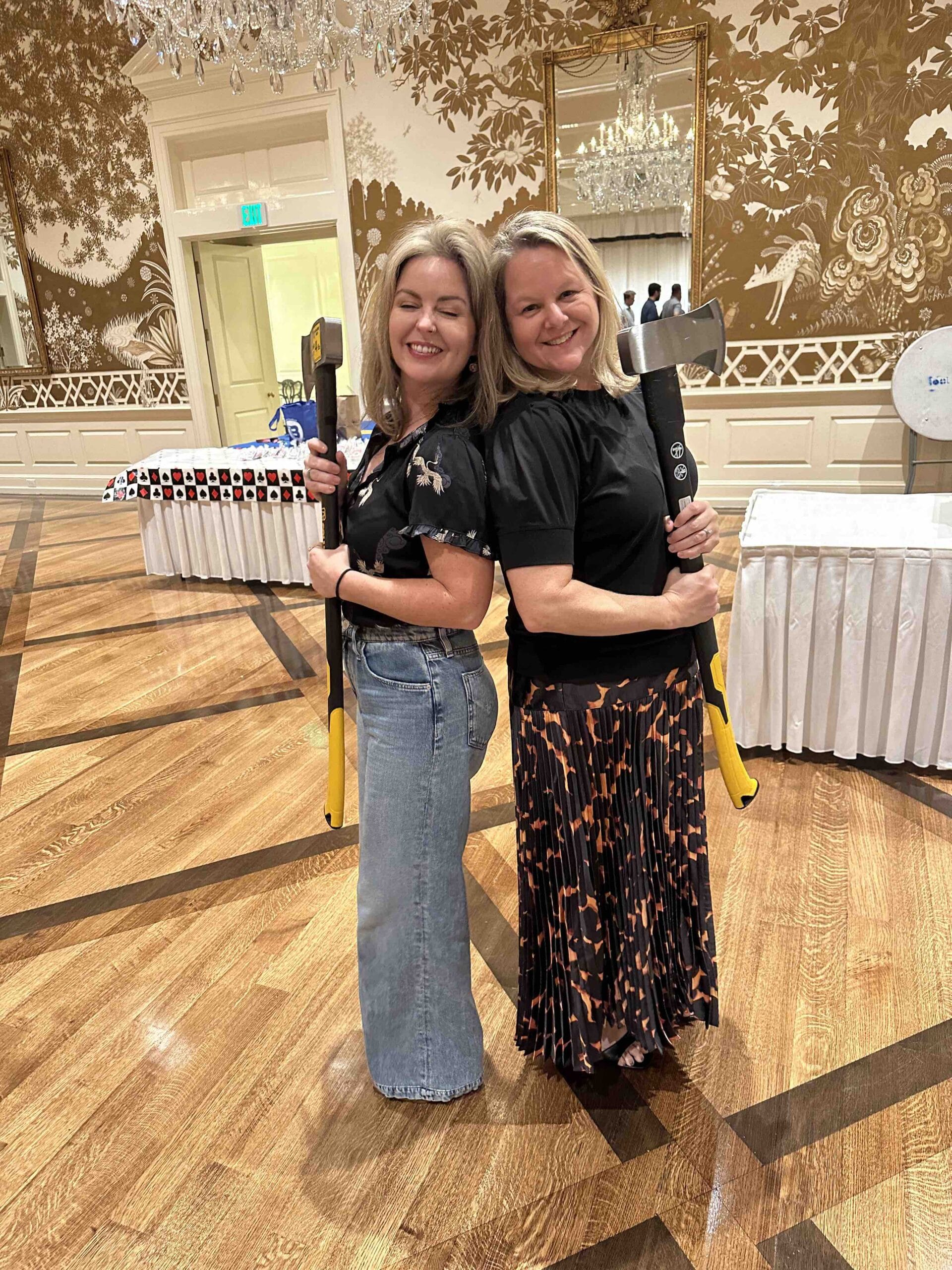 Two Houston Toolbank ladies standing back to back holding axes in a ballroom