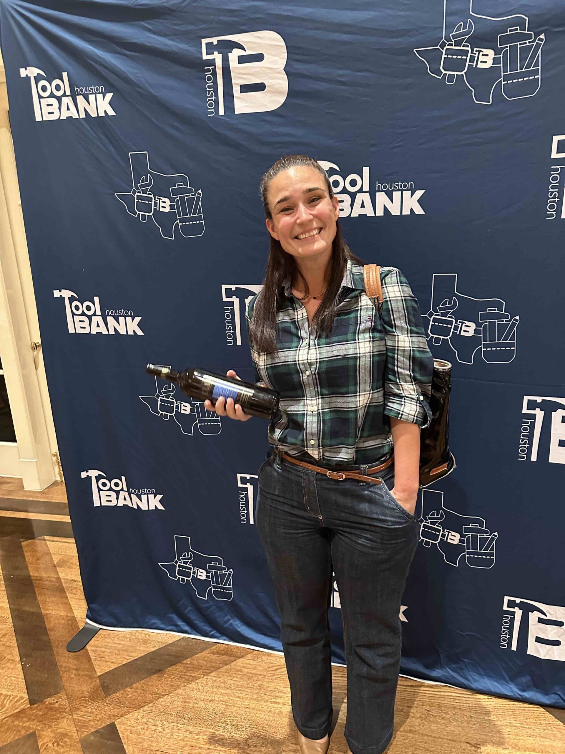 A Houston Toolbank team member holding a winning bottle and smiling against a Toolbank backdrop