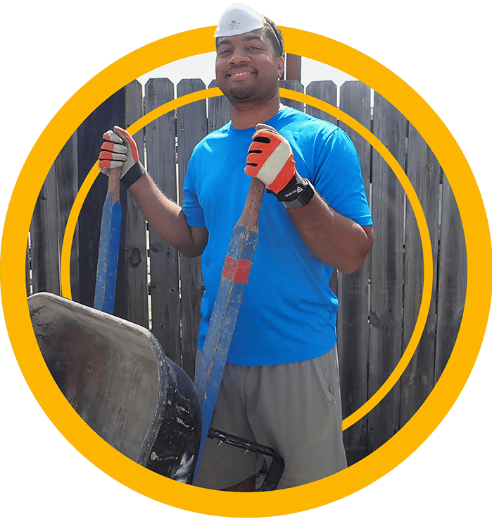 A Houston ToolBank volunteer with orange gloves holding up wheelbarrow handles and smiling