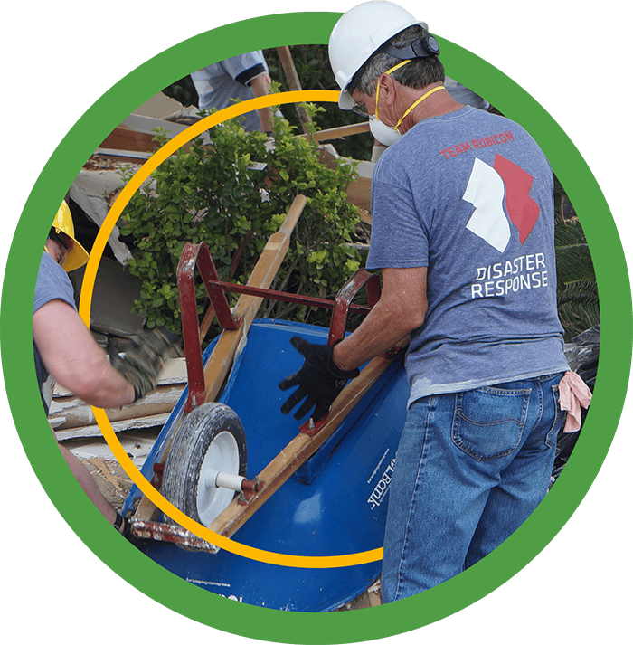 A green badge of a Rubicon disaster volunteer dumping a blue Houston ToolBank wheelbarrow